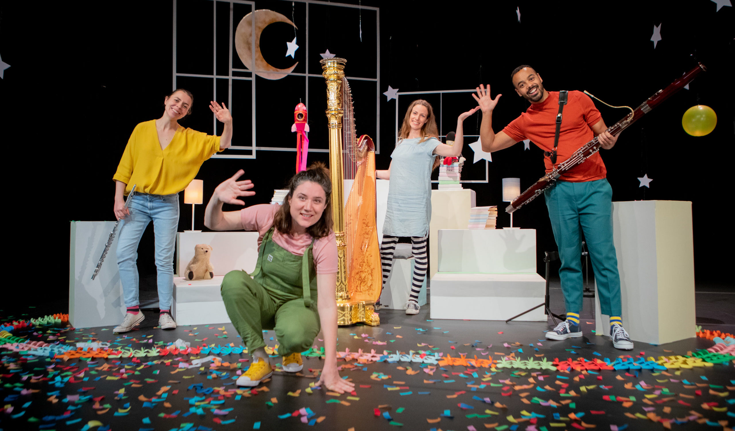Four adults wave at the camera, surrounded by children's props and colourful scenery