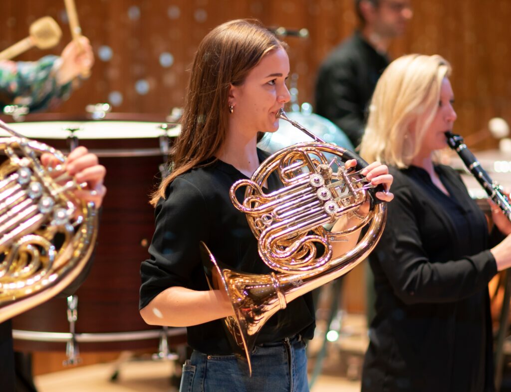 A woman plays the French horn on the Royal Festival Hall stage